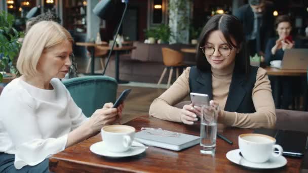İş yemeği sırasında kafede akıllı telefon kullanan kadın meslektaşlar ekrana dokunuyor. — Stok video