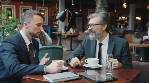 Радостные коллеги разговаривают и смеются, расслабляясь в кафе во время кофе-брейка — стоковое видео