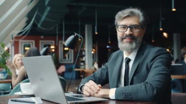 Cafe 'de dizüstü bilgisayarlı ciddi yüzlü kameraya bakan yakışıklı iş adamının portresi.