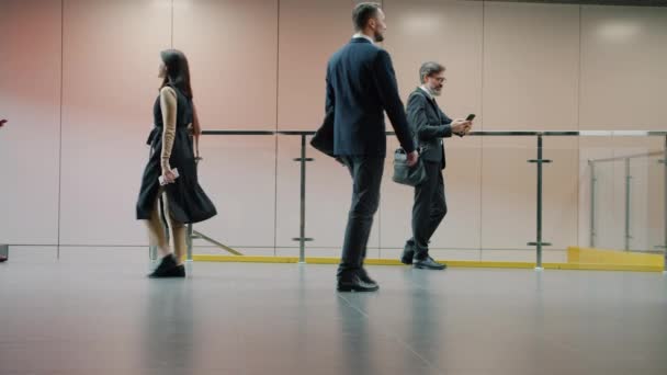 Медленное движение людей, идущих по коридору в костюмах, женщин, катающихся чемоданах — стоковое видео