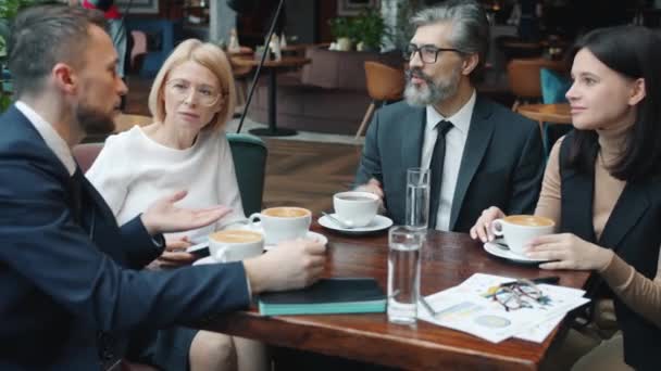Веселые мужчины и женщины деловые партнеры в костюмах разговаривают улыбаясь в ресторане — стоковое видео