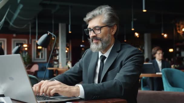 Érett vállalkozó, aki laptopot használ az étteremben gépelés az asztalnál egyedül — Stock videók