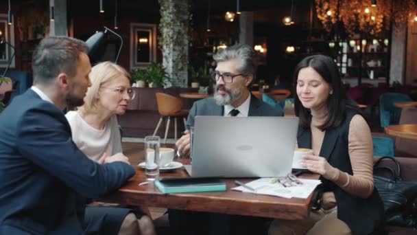 Jeunes et matures hommes d'affaires discuter du projet dans le restaurant en utilisant l'ordinateur à la table — Video