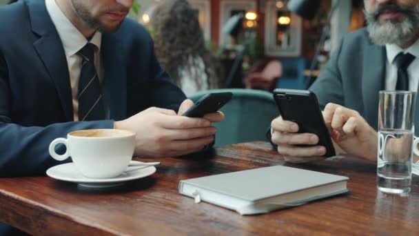 Primer plano de los hombres de negocios que utilizan teléfonos inteligentes que tocan la pantalla en el restaurante — Vídeo de stock