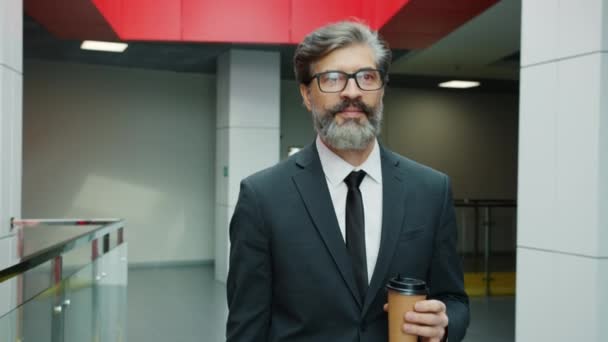 Медленное движение красивого зрелого мужчины, идущего по коридору офисного центра, держащего кофе — стоковое видео
