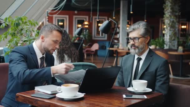 Злий підприємець кричить на колегу-чоловіка кидаючи папери за столом у кафе — стокове відео