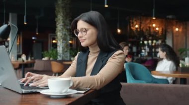 Genç çekici iş kadını restoranda tek başına dizüstü bilgisayar kullanıyor.