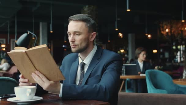 Joven hombre de negocios inteligente leyendo libro relajándose en la mesa en el restaurante solo — Vídeo de stock