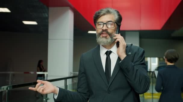 Zwolniony ruch dojrzałego biznesmena rozmawiającego przez telefon komórkowy spacerującego w holu z kciukami w górze — Wideo stockowe