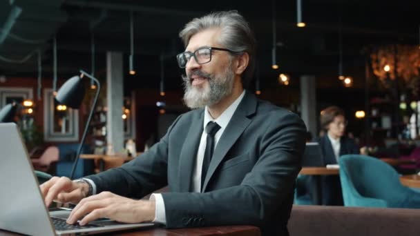 Зрелый бизнесмен разговаривает и жестикулирует с помощью ноутбука в кафе — стоковое видео