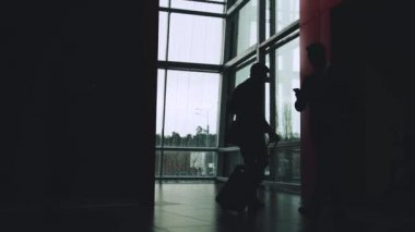 Lobide yürüyen ofis çalışanlarının siluetleri, yolda giderken bavulu yuvarlayan adamlar.