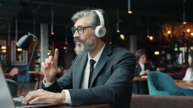 Cafede dizüstü bilgisayar kullanan neşeli bir ofis çalışanı müzik dinliyor ve restoranda şarkı söylüyor.