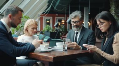 Erkek ve kadın meslektaşlar akıllı telefon kullanır sonra da kafede içeriği tartışırlar.