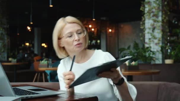 Elegante mujer de negocios haciendo videollamada en línea en el café hablando mostrando gráfico utilizando el ordenador portátil — Vídeos de Stock