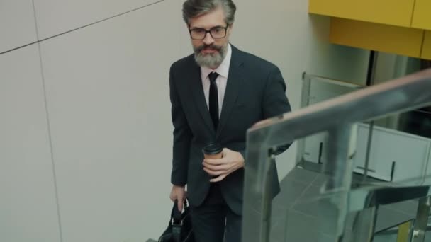 Mature business man walking in lobby of office center holding suit and take out coffee — Stock Video