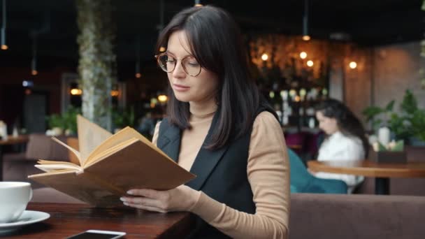 Intelligent ung kvinna i eleganta formalwear njuter bok läsning på café — Stockvideo