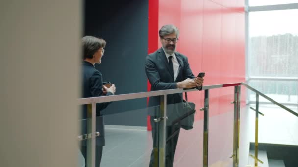 Empresario usando smartphone en lobby estrechando la mano con compañero de trabajo hablando — Vídeo de stock