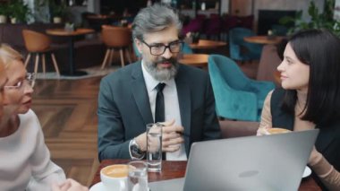 Bir grup iş adamı resmi giysiler içinde restoranda bilgisayar kullanarak konuşuyor.
