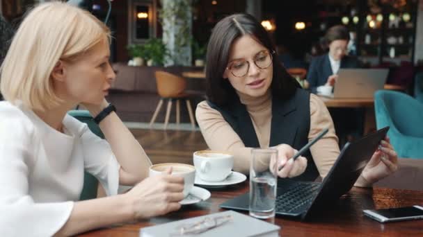 Female business partners talking pointing at laptop screen in restaurant