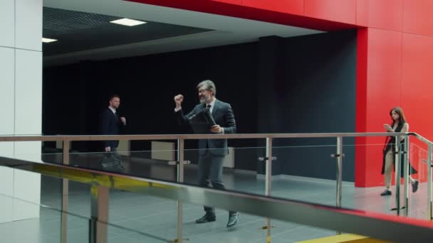 Зрілий чоловік в костюмі танцює в офісному коридорі, насолоджуючись успішною роботою і досягненнями в бізнесі — стокове відео