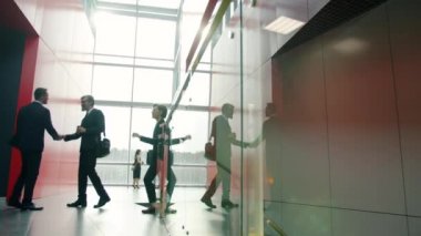 Resmi giyinmiş ofis çalışanları lobide el sıkışıyorlar.