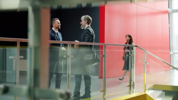 Male colleagues in formal clothing talking in office lobby while businesswomen walking around — Stock Video