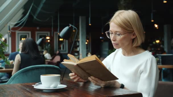 Akıllı iş kadını, olgun sarışın, restoranda kitap okuyor, dinleniyor. — Stok video