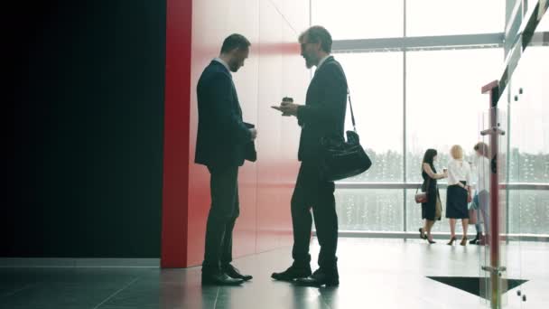 Businessmen talking in office center hall discussing work then waving hands and leaving — Stock Video