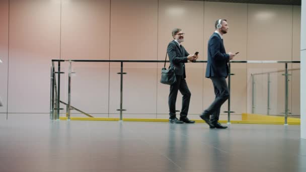 Повільний міф про бізнесмена, використовуючи смартфон у вестибюлі, поки колеги рухаються навколо — стокове відео