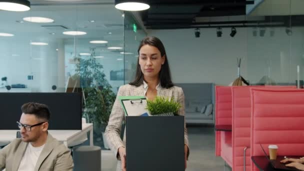 Smutna młoda kobieta wychodząca z pracy z pudełkiem rzeczy spacerujących w biurze na otwartej przestrzeni — Wideo stockowe