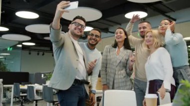 Çok ırklı bir ekip, ortak çalışma alanında akıllı telefonlu selfie çekerek gülümsüyor.