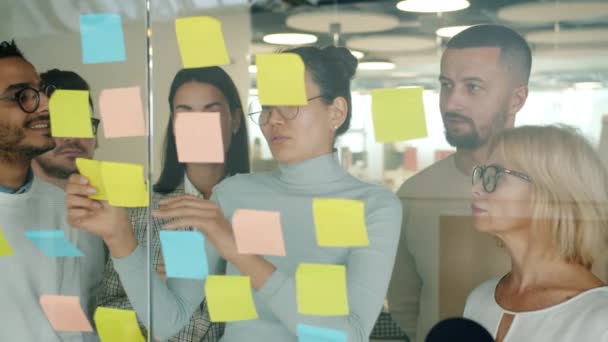 Gente de negocios que trabaja con notas adhesivas en la oficina usando paneles de vidrio hablando — Vídeo de stock