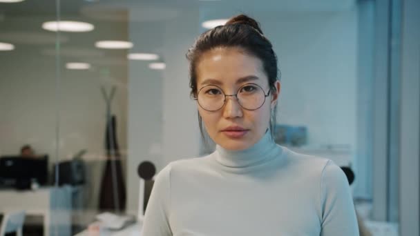 事務所に立ってカメラを見る眼鏡の中の深刻なアジアのオフィスワーカーの肖像画 — ストック動画