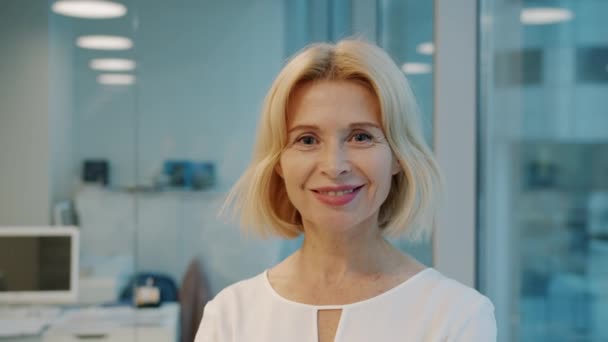 Portrait of elegant mature businesswoman smiling in office looking at camera — Stock Video