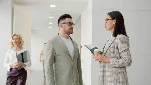 Girl and guy colleagues talking in office hall while people walking around — Stock Video