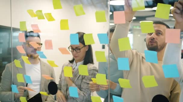 Movimiento lento de compañeros de trabajo que trabajan con notas adhesivas coloridas lluvia de ideas en la oficina — Vídeo de stock