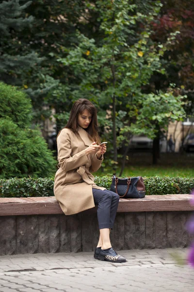 Young beautiful woman sitting on a bench in the autumn park — Stock Photo, Image