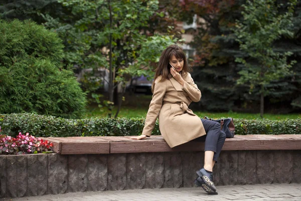 Young beautiful woman sitting on a bench in the autumn park — Stock Photo, Image