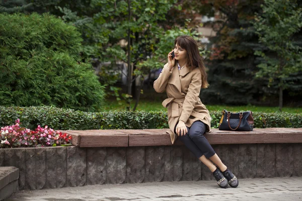 Jeune belle femme assise sur un banc dans le parc d'automne — Photo