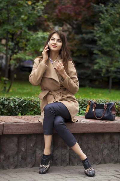 Mladá krásná žena sedící na lavičce v podzimní park — Stock fotografie