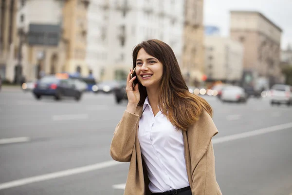 Portrait de heureuse jeune femme brune en manteau beige parlant sur — Photo