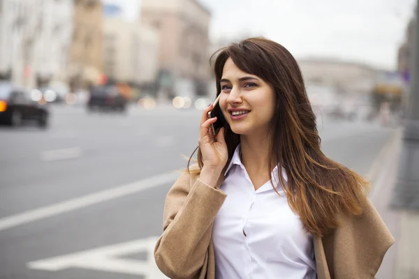 Portrait of happy young brunette woman in beige coat talking on — Stock Photo, Image