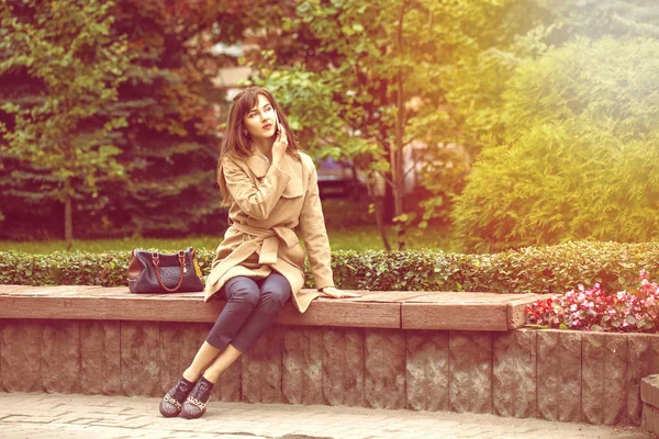Joven hermosa mujer sentada en un banco en el parque de otoño — Foto de Stock