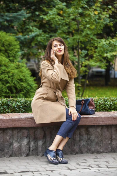 Mladá krásná žena sedící na lavičce v podzimní park — Stock fotografie
