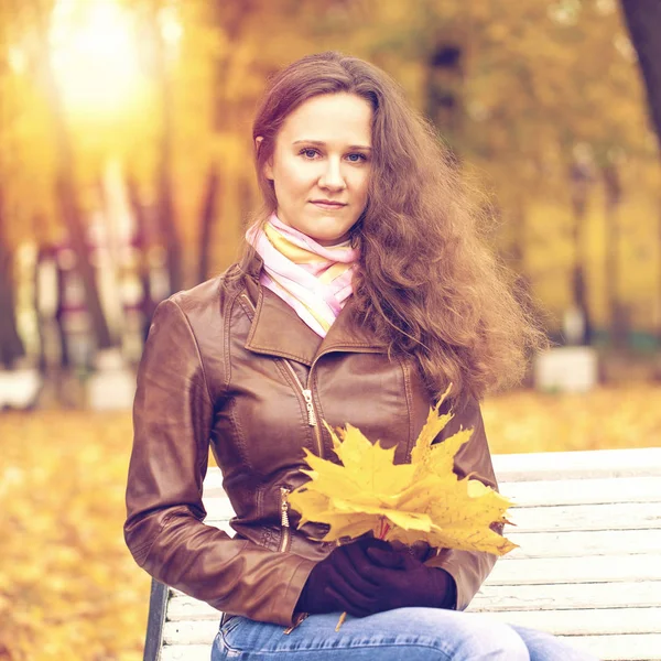 Jovem mulher sentada no banco no parque de outono — Fotografia de Stock