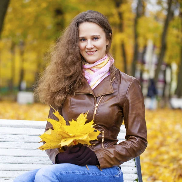 Mujer joven sentada en el banco en el parque de otoño — Foto de Stock