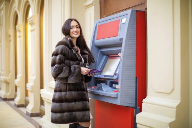 Happy brunette woman withdrawing money from credit card at ATM  clipart