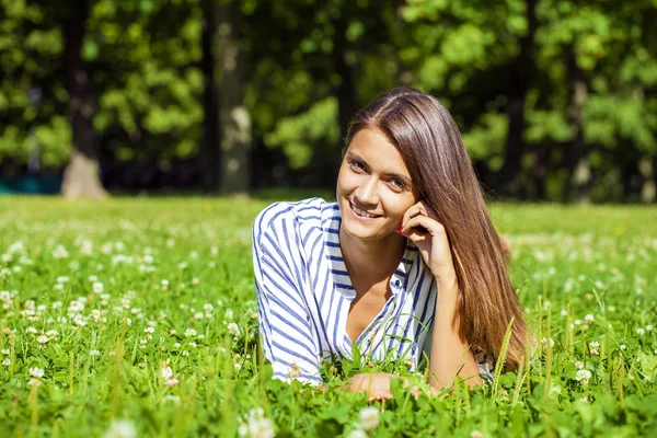 Aantrekkelijke jonge brunette vrouw liggend op groen grasveld op su — Stockfoto