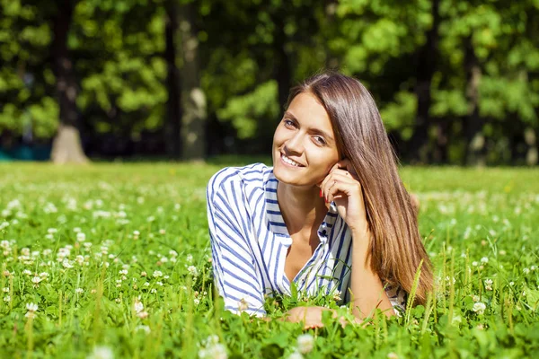 Attractive young brunette woman lying on green grass field at su — Stock Photo, Image