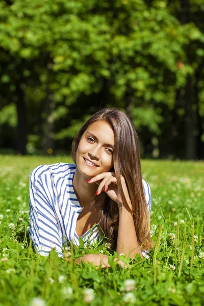 Attractive young brunette woman lying on green grass field at su — Stock Photo, Image